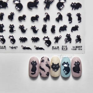 May include: Sheet of black cat nail art stickers with various cat poses. Below are five painted nails with cat designs, including a black cat silhouette, paw prints, and a cat face. The nails are painted in shades of pink, beige, and blue.