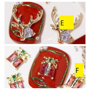 Pode incluir: Conjunto de decora&ccedil;&otilde;es para unhas com tema natalino. As decora&ccedil;&otilde;es incluem um veado dourado com um strass transparente, uma caixa de presente dourada com um strass vermelho e verde, e uma caixa de presente dourada com um strass verde. As decora&ccedil;&otilde;es est&atilde;o sobre um fundo vermelho com detalhes verdes e brancos.
