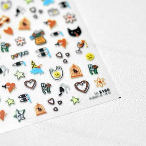 Könnte beinhalten: Ein Bogen dekorativer Aufkleber mit verschiedenen farbenfrohen Designs. Die Aufkleber umfassen Herzen, Sterne, Blumen, Vögel in Käfigen, Katzenköpfe und andere skurrile Illustrationen. Die Aufkleber befinden sich auf einem klaren, transparenten Hintergrund.