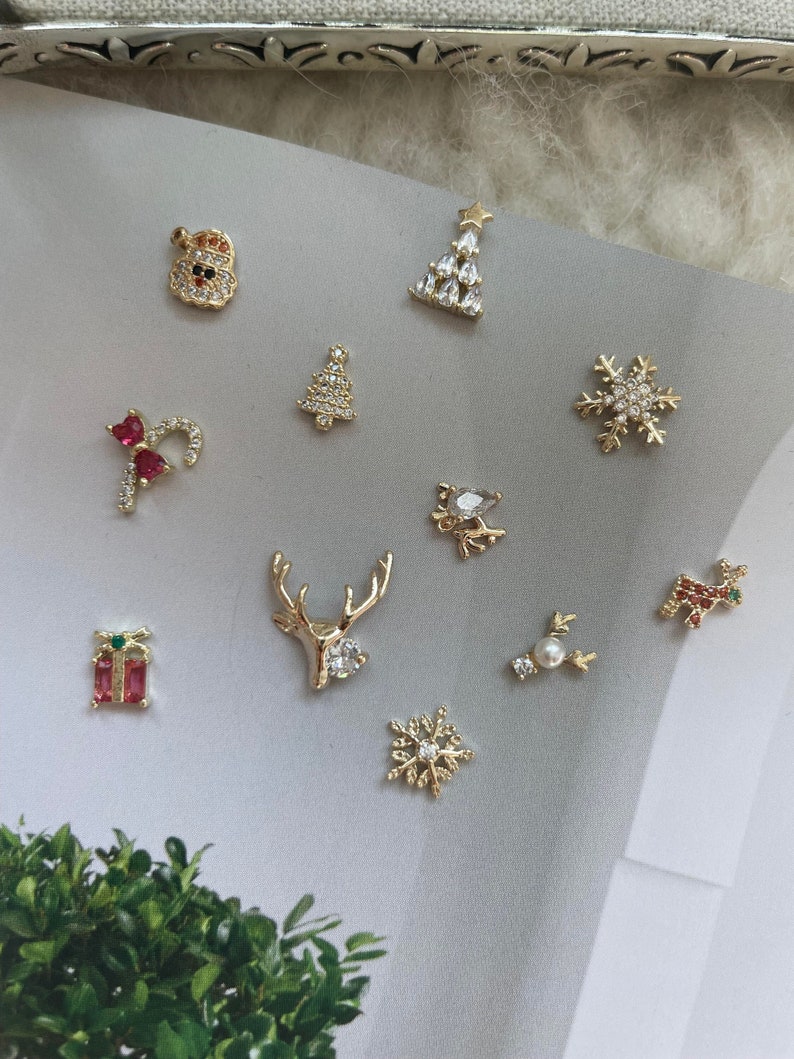Pode incluir: Conjunto de pingentes para unhas com tema natalino em tom dourado. Os pingentes incluem um boneco de neve, uma &aacute;rvore de Natal, um bast&atilde;o de caramelo, uma rena, um floco de neve, uma caixa de presente e uma estrela.
