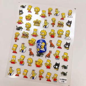May include: Sheet of nail art stickers featuring cartoon characters, including Bart, Lisa, and Homer Simpson. The stickers are yellow, red, and black, with some angel-themed designs. A blue sticker with the text "It's OK" is also present.
