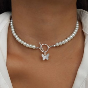May include: A white pearl choker necklace with a silver butterfly pendant. The necklace has a toggle clasp.