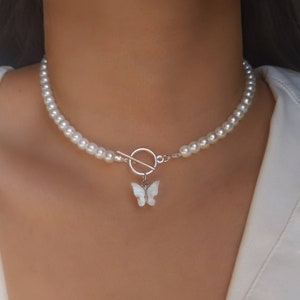 Op de afbeelding: Een witte parel choker ketting met een zilveren schuifgesp en een witte vlinder hanger.
