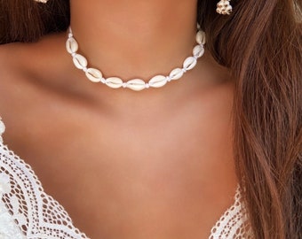 Puede incluir: Un collar choker de conchas blancas con un cordón blanco delicado. El collar está hecho de pequeñas conchas ovaladas.