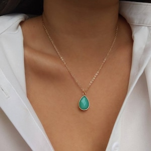 Pode incluir: Um colar de corrente de ouro com um pingente em forma de lágrima com uma gema verde.
