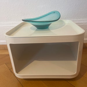 May include: White side table with a single shelf and a teal blue glass bowl on top.