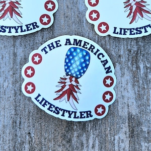 May include: Four white round stickers with a red, white, and blue pineapple design. The text "The American  Lifestyler" is written around the pineapple on each sticker.