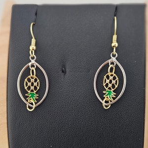 May include: A pair of gold and silver earrings with a green and white pineapple design.