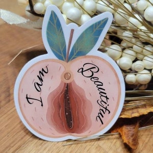 May include: A peach-colored sticker with a stylized image of a peach cut in half. The text "I am Beautiful" is written inside the peach.