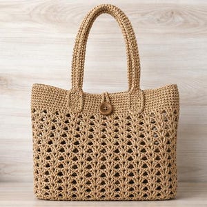 Puede incluir: Un bolso tote de color tostado con un intrincado patrón de ganchillo calado en todo el cuerpo. El bolso incluye dos asas superiores resistentes y un cierre de botón de madera marrón centrado en el borde superior para asegurar la abertura.