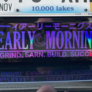 May include: A black car with a sticker that reads "Early Mornings" in a purple and blue iridescent font. The sticker also includes the text "Grind. Earn. Build. Succeed." and Japanese text.