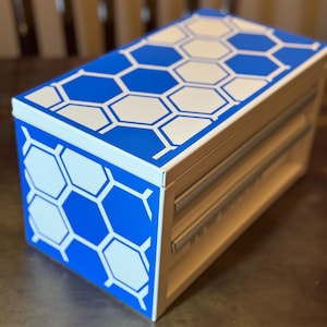 May include: A white toolbox with three drawers, featuring a blue and white honeycomb pattern on the top.