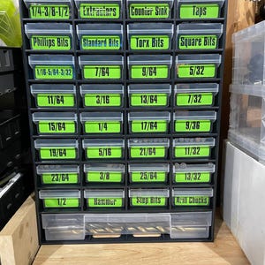 May include: A black plastic drawer organizer with green labels for different drill bit sizes. The labels include sizes like 1/4, 3/16, 5/16, 3/8, 7/64, 9/64, 11/64, 13/64, 15/64, 17/64, 19/64, 21/64, 23/64, 25/64, 5/32, 7/32, 9/36, 11/32, 13/32, 1/2, and 1/4-3/8-1/2. The drawer organizer also has labels for "Extractors", "Counter Sink", "Taps", "Phillips Bits", "Standard Bits", "Torx Bits", "Square Bits", "Hammer", "Step Bits", and "Drill Chucks".