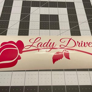 May include: A pink vinyl decal with a rose and the text "Lady Driven".