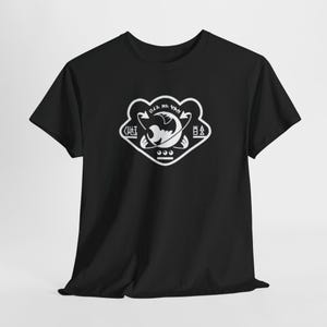 May include: Black t-shirt featuring a white graphic design. The design includes a stylized emblem with curved lines, shapes, and symbols. The shirt is made of a soft material and has short sleeves.