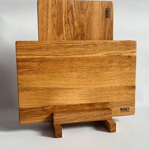 May include: Two wooden cutting boards with a natural wood grain finish. The larger board rests on a small stand, and the smaller board is placed behind it. The boards have the text "WOODDEY WORKSHOP" printed on them.
