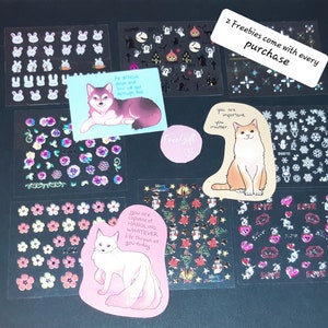 May include: Assortment of colorful stickers featuring various designs, including animals, flowers, and inspirational quotes. The stickers are arranged on a black surface. The text on the stickers reads: "No difficult days and you will get through this", "Free Gift", "You are important. You matter.", "You are capable of handling whatever life throws at you today", and "2 Freebies come with every purchase".