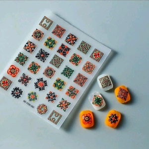 May include: A sheet of clear silicone with 25 individual moulds of geometric designs in orange, black, and green. The sheet is labelled "SD FEB-382". There are 7 separate silicone moulds with the same geometric designs in orange, black, and green.