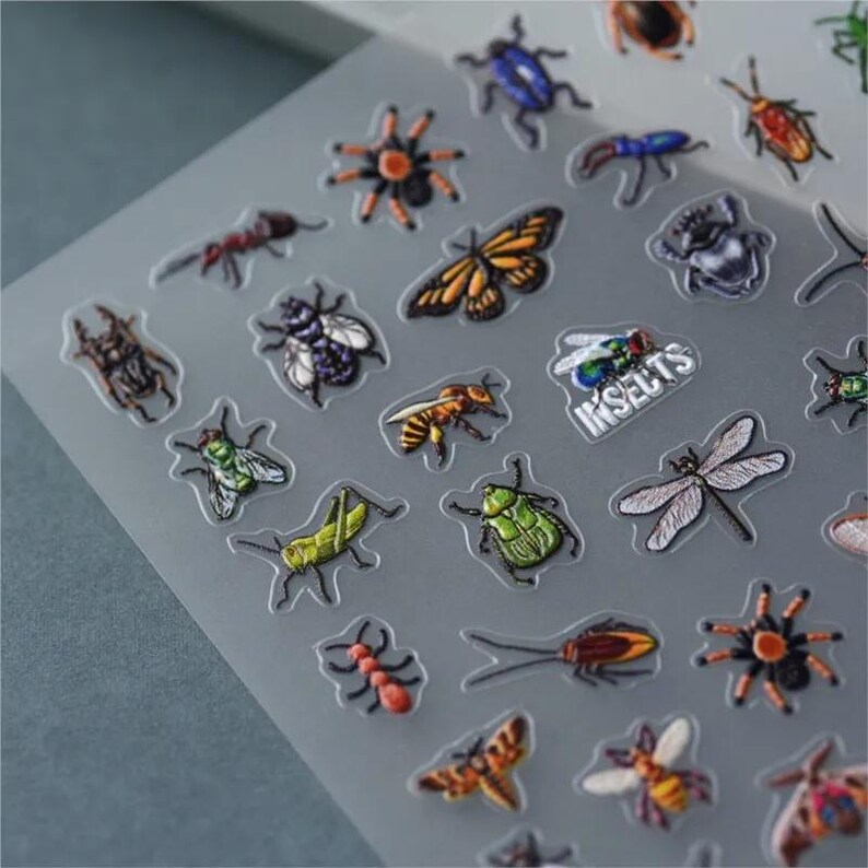 May include: A sheet of clear vinyl stickers featuring various insects, including butterflies, spiders, ants, beetles, and dragonflies. The stickers are printed with colorful, detailed illustrations and the word "INSECTS" is printed in white on the sheet.