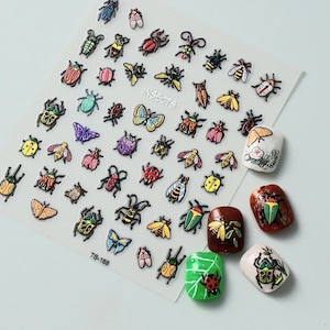 May include: A sheet of nail art stickers with insect designs, including beetles, butterflies, and bees in various colours. The sheet has the text "INSECTS" and "TS-168". Several decorated fingernails are also visible.