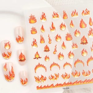 May include: A sheet of nail art stickers featuring a variety of orange and yellow flame designs. The sheet includes different flame shapes and sizes, including a campfire design. The sheet is labelled "TS-224".