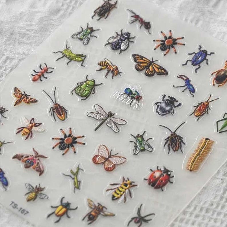 May include: A sheet of colorful insect stickers with a variety of designs, including butterflies, beetles, dragonflies, and spiders. The stickers are arranged in a grid pattern on a white background. The text "INSECTS" is printed in the center of the sheet.