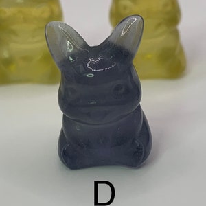 May include: A dark gray, translucent, rabbit-shaped figurine with a letter "D" printed below it.