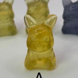 May include: A yellow gummy candy shaped like a rabbit. The candy has a translucent appearance and is sitting on a white surface.