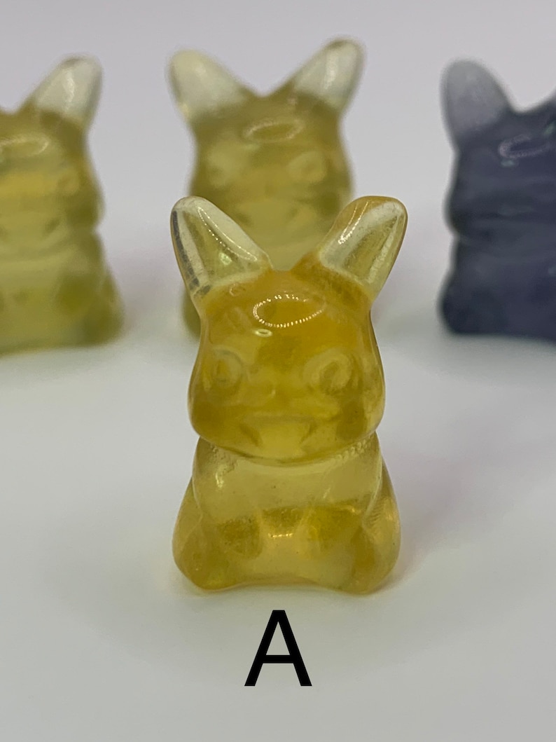 May include: A yellow gummy candy shaped like a rabbit. The candy has a translucent appearance and is sitting on a white surface.
