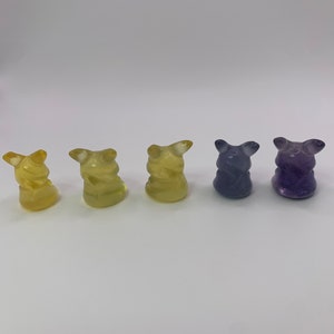 May include: Five small figurines, each with a different color. The figurines are yellow, yellow, yellow, purple, and purple. They are all in the shape of a small animal with a rounded body and a pointed head.