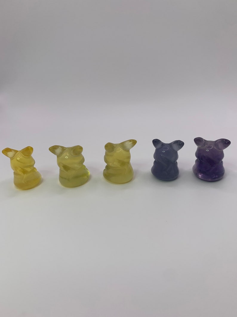 May include: Five small figurines, each with a different color. The figurines are yellow, yellow, yellow, purple, and purple. They are all in the shape of a small animal with a rounded body and a pointed head.