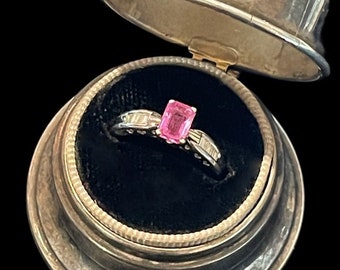 May include: A pink gemstone ring with a silver band and small diamonds set in the band. The ring is in a silver ring box.