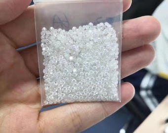 May include: A clear plastic bag filled with numerous small, clear, faceted gemstones. The bag is held in a person's hand, with the gemstones appearing to sparkle. The bag is sealed at the top.
