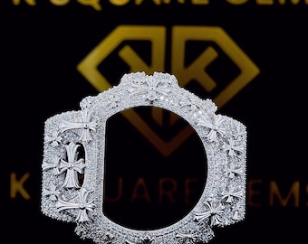 May include: A silver-colored, ornate watch bezel with a cross design. The bezel is encrusted with small, sparkling stones and features the text "K SQUARE GEM" in gold lettering on a black background.