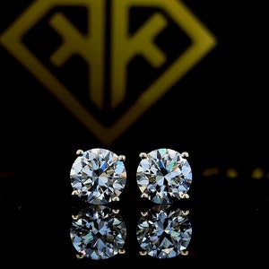 以下が含まれることがあります： 金色の枠にセットされた、丸い透明なダイヤモンドのスタッドピアスのペア。ピアスは黒い背景に置かれています