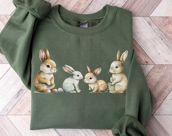 May include: A green sweatshirt with a graphic of four bunnies. The bunnies are brown and white and are arranged in a line. The sweatshirt has a crew neck and long sleeves.