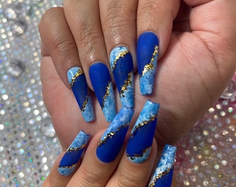 May include: Blue and white marble design nail polish with gold glitter accents on long, almond-shaped nails.