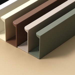 Può includere: Primo piano di una serie di elementi architettonici rettangolari in metallo di vari colori. I colori includono nero, bianco, crema, marrone, beige e verde oliva. Gli elementi hanno un bordo superiore curvo e una base piatta.