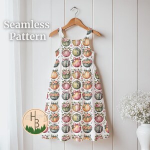 May include: A sleeveless white dress with a pumpkin pattern, hanging on a wooden hanger. The dress features a repeating pattern of colorful pumpkins adorned with bows and flowers. The words "Seamless Pattern" are in the upper left corner.