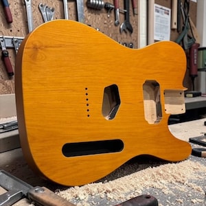 Peut inclure: Un corps de guitare électrique non fini avec une finition en grain de bois de couleur ambre vif. Le corps présente des cavités prédécoupées pour les micros et le chevalet, ainsi qu'une série de petits trous pour les ferrules sur la face avant.