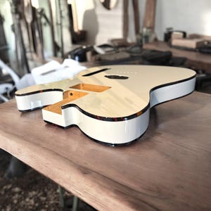 Peut inclure: Un corps de guitare électrique non fini avec une finition crème brillante et un filet de bordure en écaille de tortue foncé. Le corps présente une cavité pour le manche et le chevalet en bois naturel, révélant le grain du bois clair.