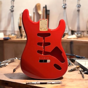 Könnte beinhalten: Rote E-Gitarrenkorpus mit einem Holzblock für die Rückplatte. Der Gitarrenkorpus steht auf einem Holztisch.