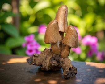 May include: A wooden sculpture of three mushrooms on a piece of driftwood. The mushrooms are brown and have a realistic appearance.