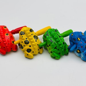 May include: Four wooden frog toys with painted details. The frogs are red, yellow, green, and blue with black spots. Each frog has a wooden handle.