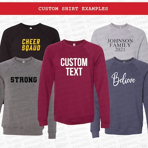 May include: A collection of raglan sleeve sweatshirts in various colors, each displaying custom text or phrases. The shirts include the phrases "CHEER SQUAD", "STRONG", "CUSTOM TEXT", "JOHNSON FAMILY 2021", and "Believe". The text is in contrasting colors.