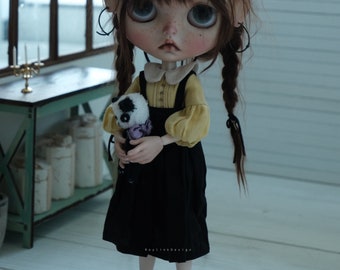 May include: A doll with brown hair in pigtails wearing a yellow blouse, black overalls, and a straw hat. The doll is holding a small stuffed panda bear. The doll is standing on a wooden floor.