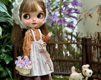 May include: A doll wearing a brown and white dress with a white crocheted hat and holding a basket of pink flowers. The doll is standing in front of a wooden fence with a small white dog sitting on the grass.