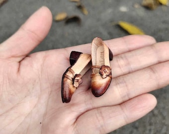 May include: A pair of brown leather doll shoes with a flower design on the front. The shoes have a small heel and are made of a soft, supple leather.
