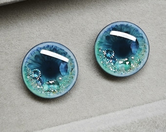 May include: Two round blue and green glass eyes with glitter and silver accents. The eyes are set against a gray background.