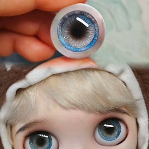 May include: A pair of blue and gray doll eyes with a white rim. The eyes have a sparkly finish and a black pupil.